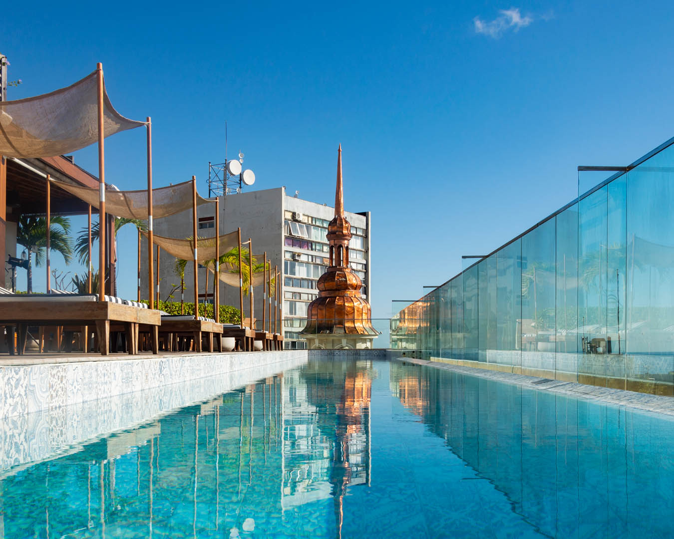 Foto em plano fechado, mostra a piscina do terraço do Fera Palace Hotel. O dia está ensolarado, as água está cristalina em tonalidade esverdeada e o céu está azul, sem nuvens.
